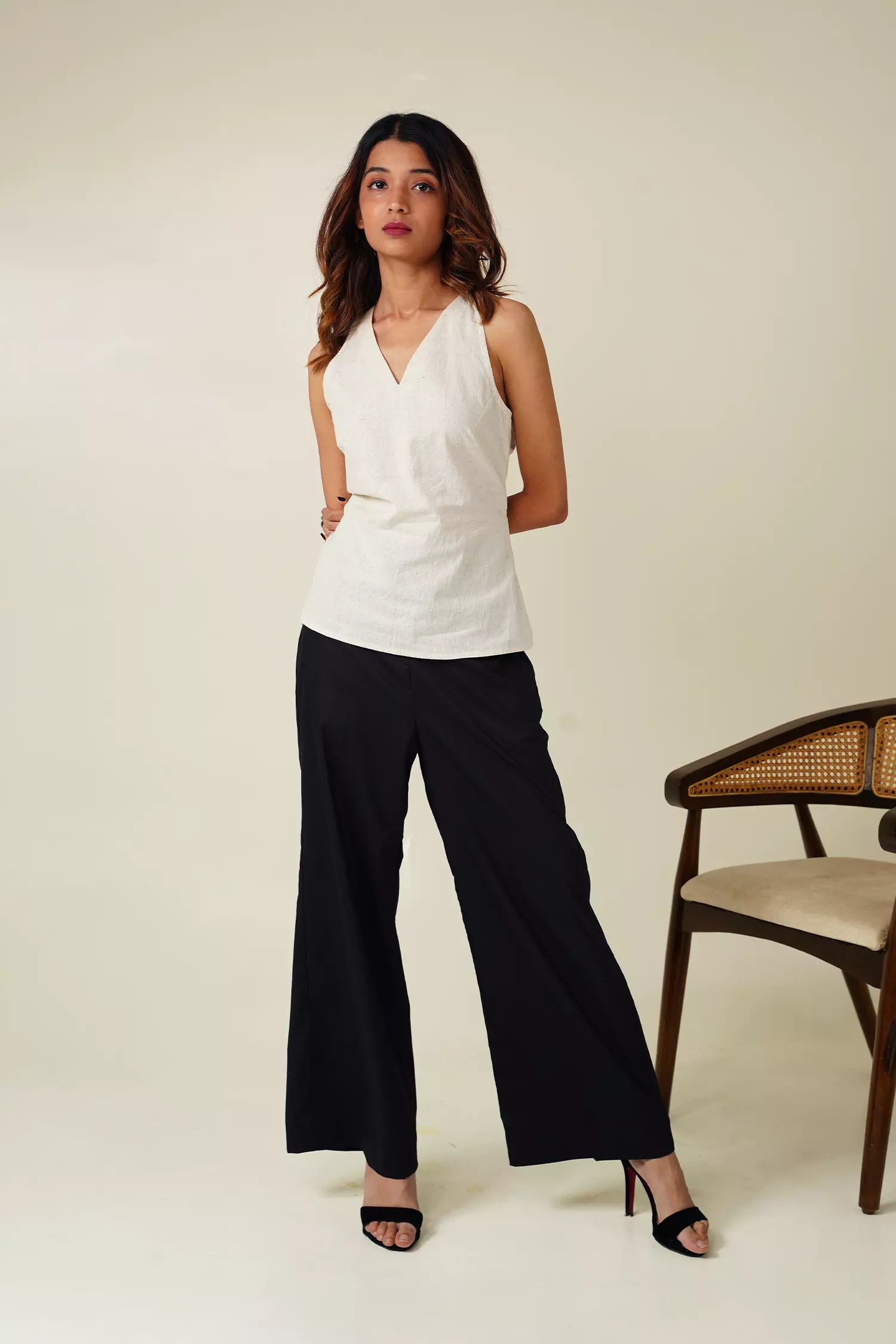front view of Woman wearing a white sleeveless top with v neckline and black pants against a neutral background