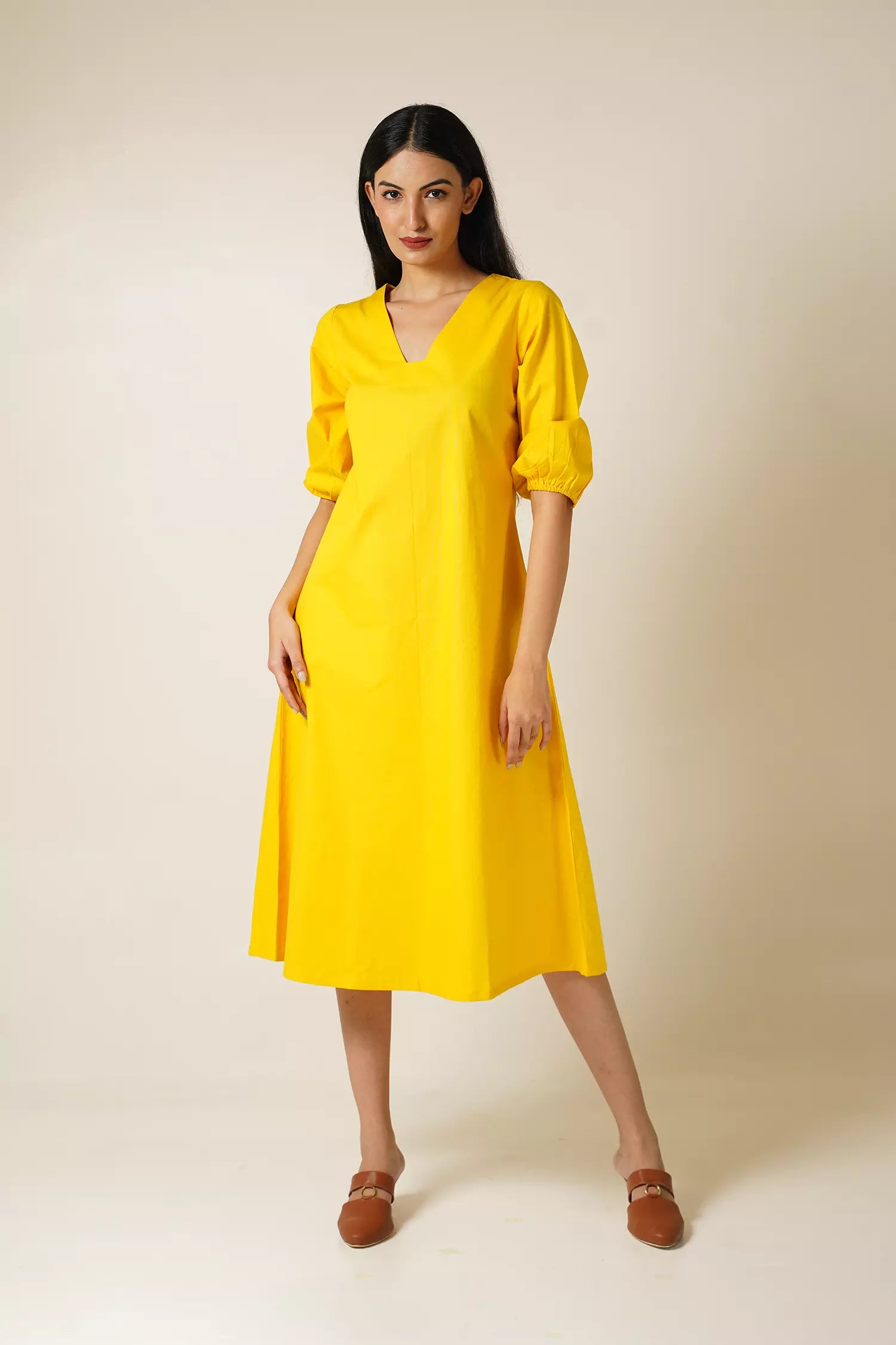 front view of a Woman wearing a cotton midi length yellow dress with v neck and puff sleeves against a plain background