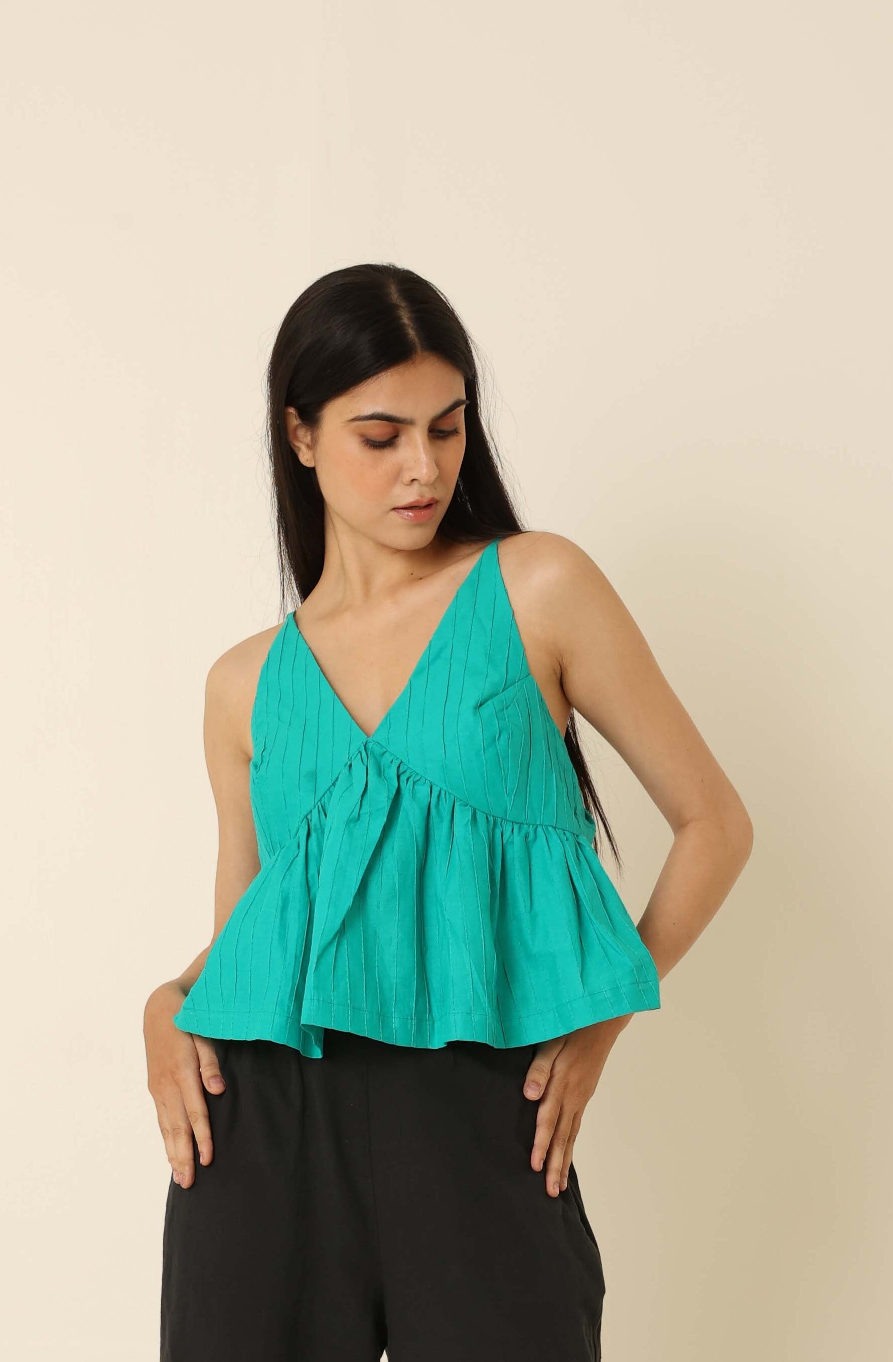 Woman wearing a green top and black pants against a beige background