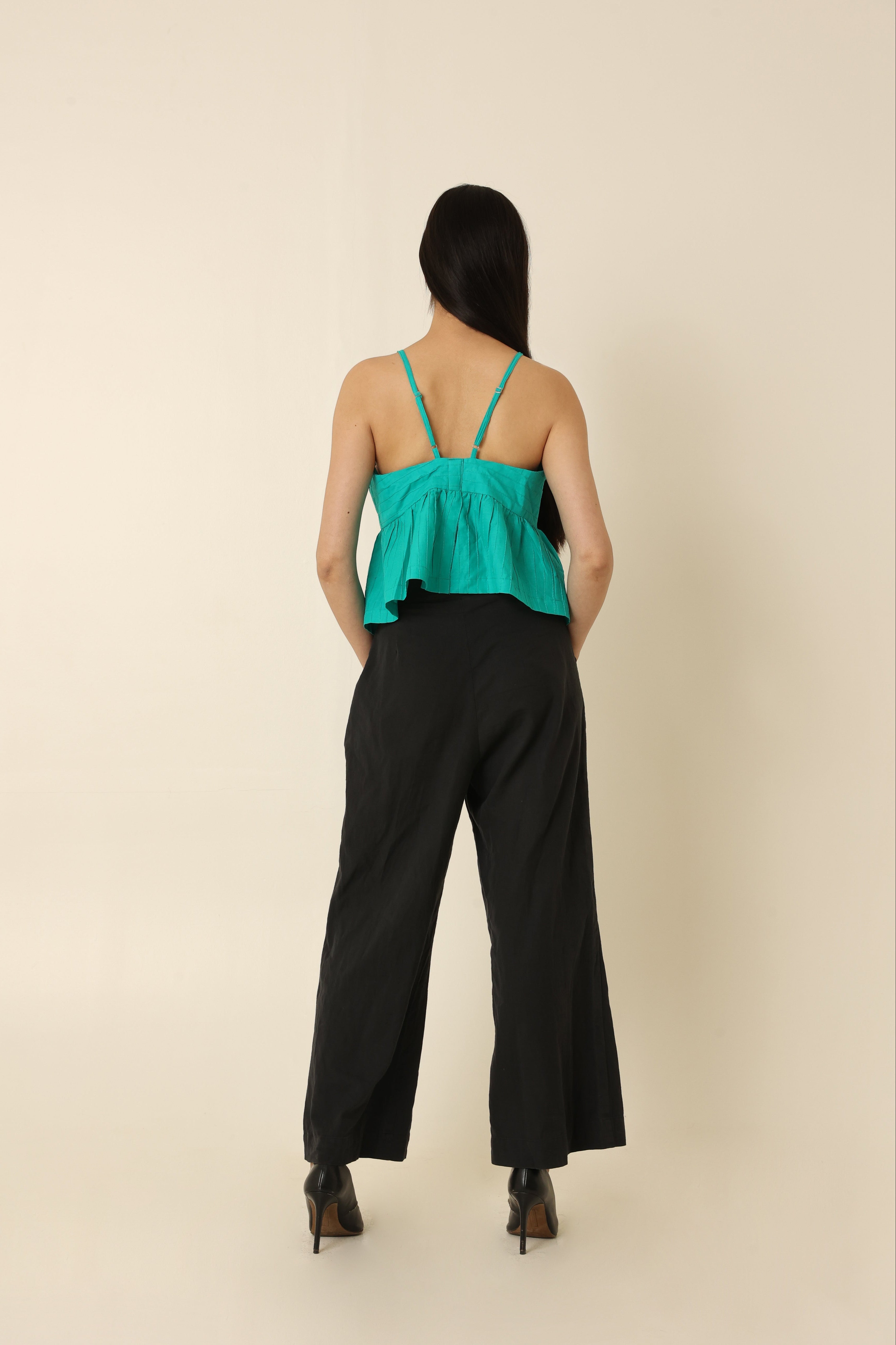 Woman wearing a green top and black pants against a beige background