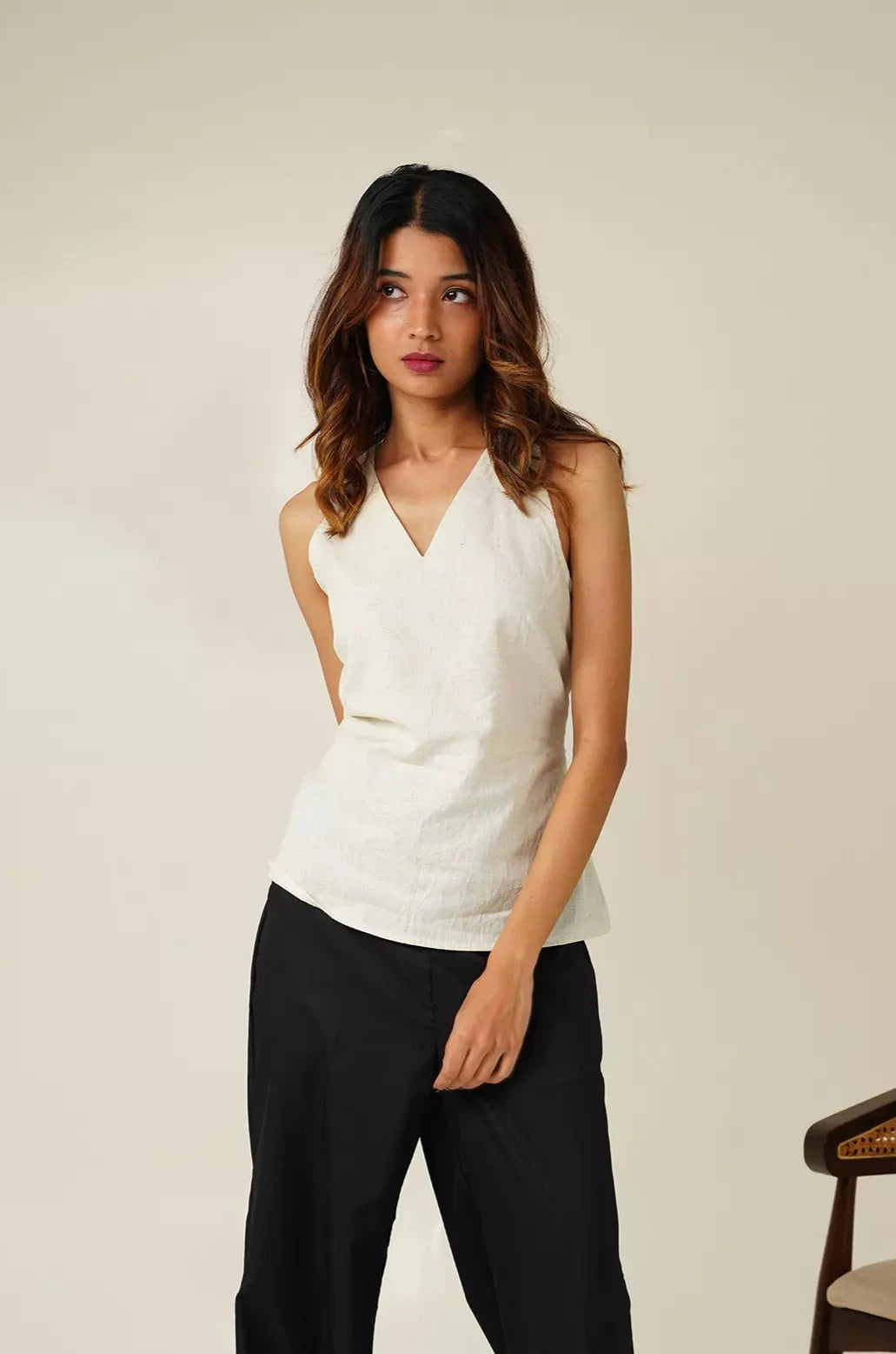 front view of Woman wearing a white sleeveless top with v neckline and black pants against a neutral background