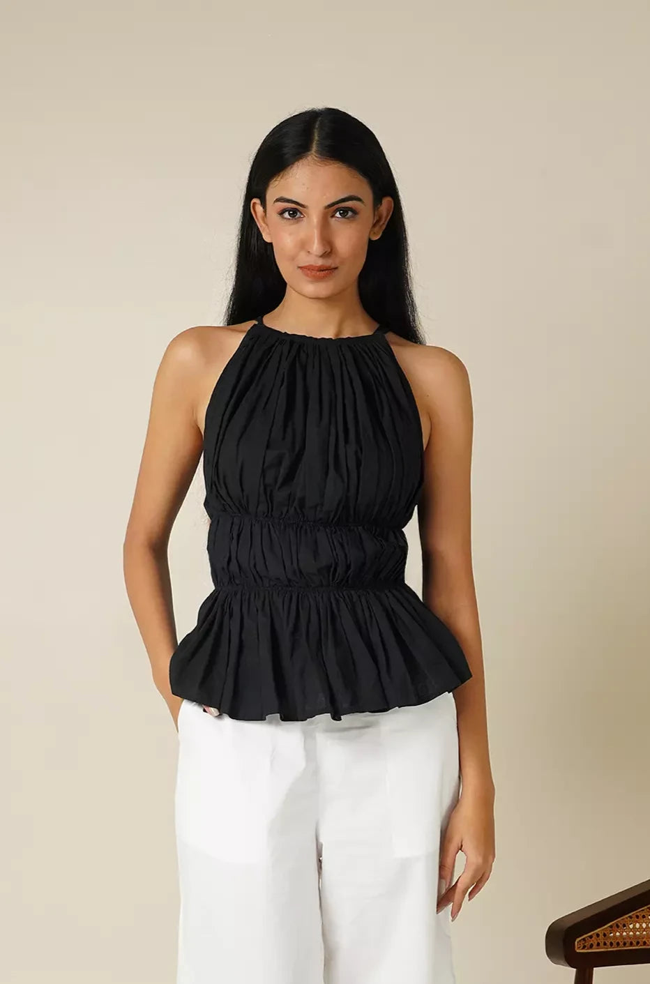 front view of Woman wearing a black sleeveless tiered top with a peplum bottom  against a beige background