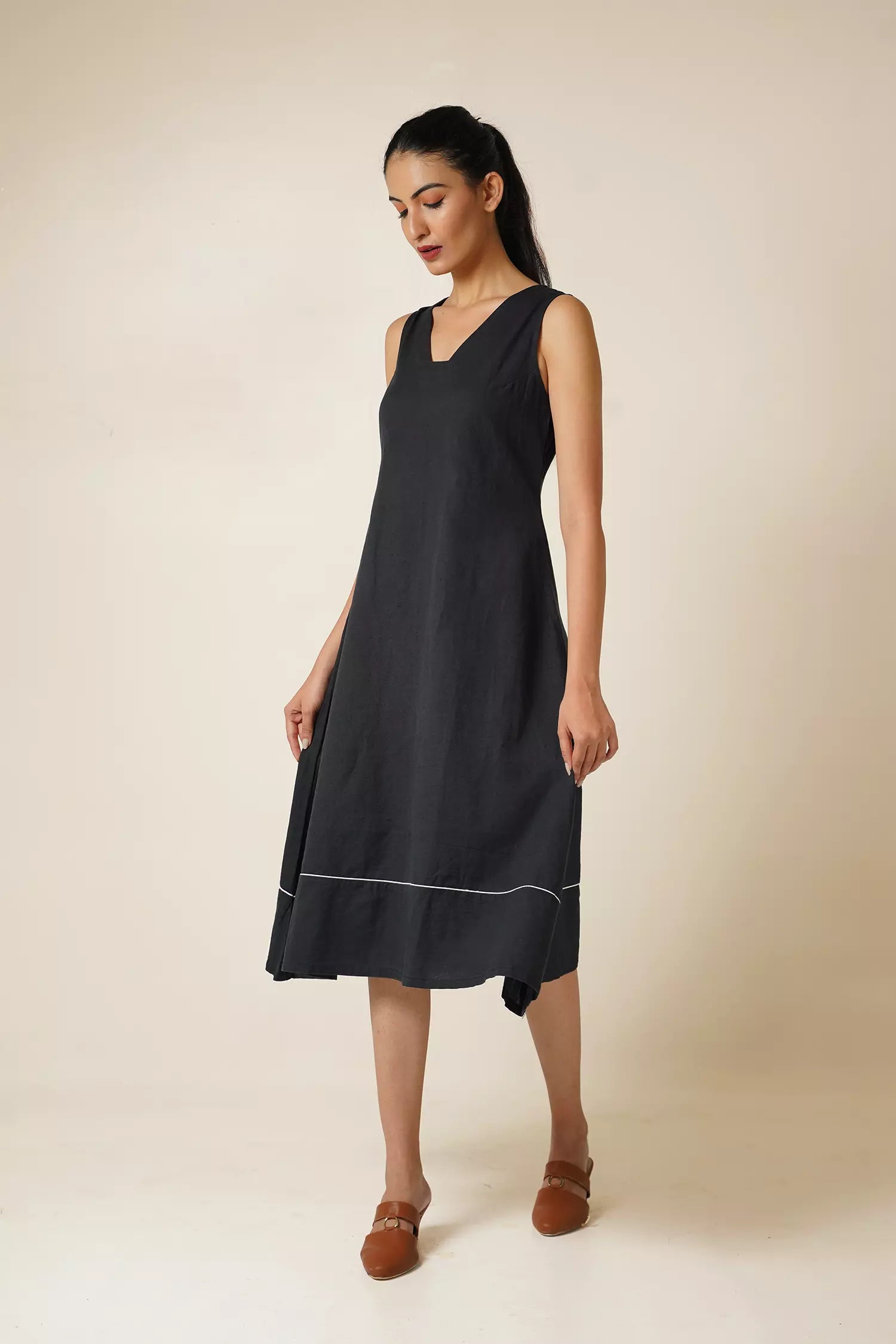 front view of Woman wearing a black knee length sleeveless dress with modified v neckline on a beige background