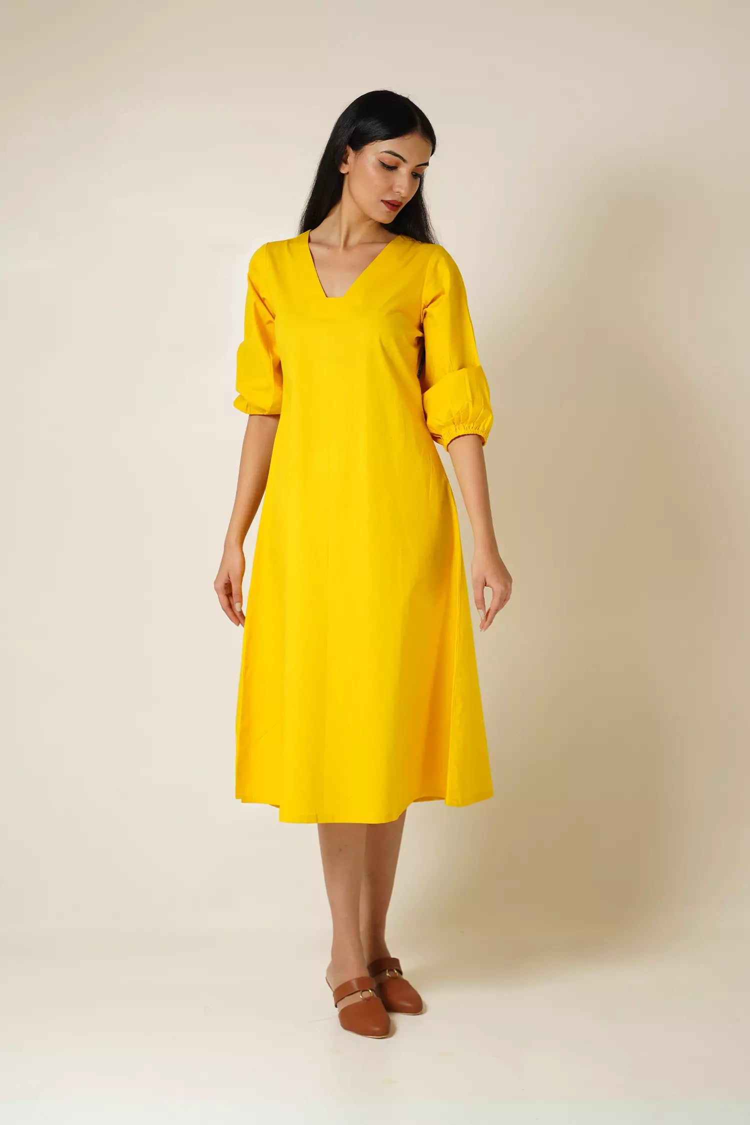 front view of a Woman wearing a cotton midi length yellow dress with v neck and puff sleeves against a plain background