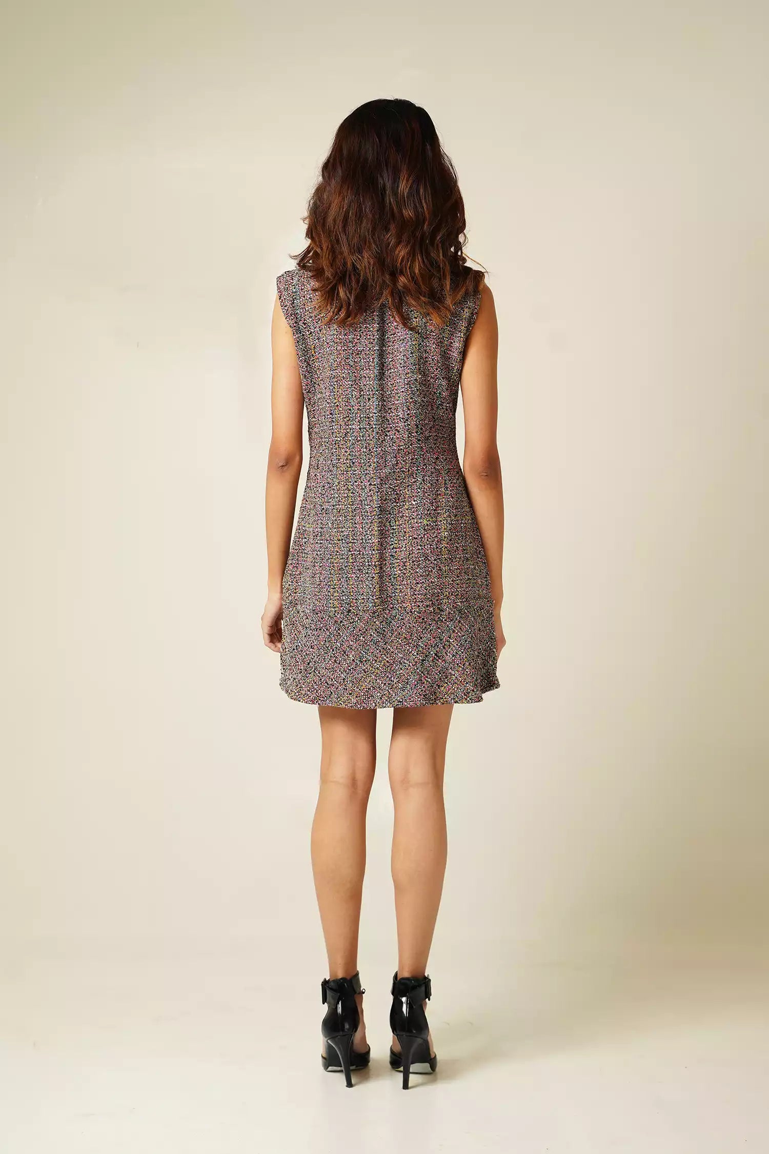 back view of Woman wearing a sleeveless multi coloured tweed mini dress on a plain background