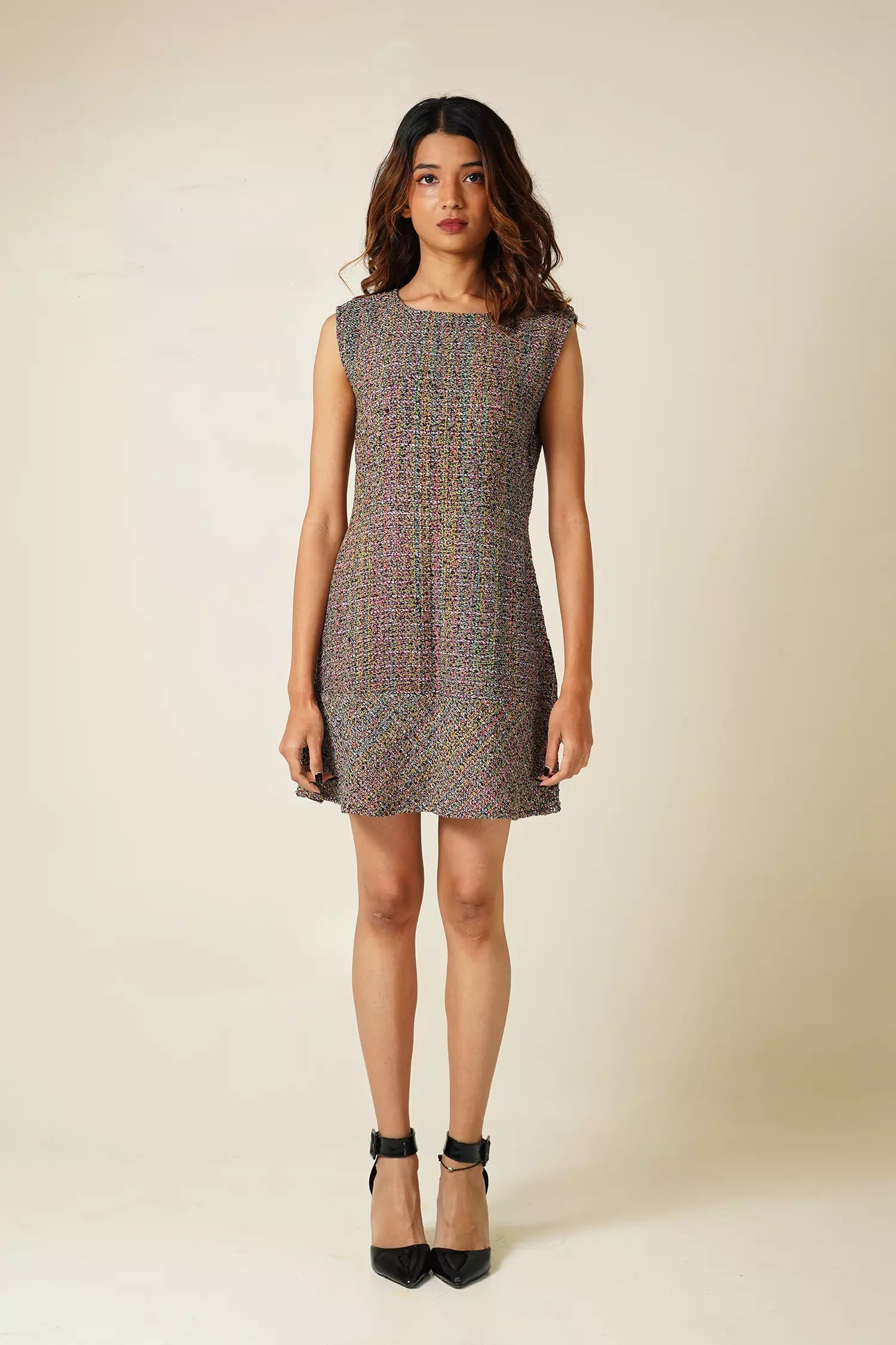 front view of Woman wearing a sleeveless multi coloured tweed mini dress on a plain background