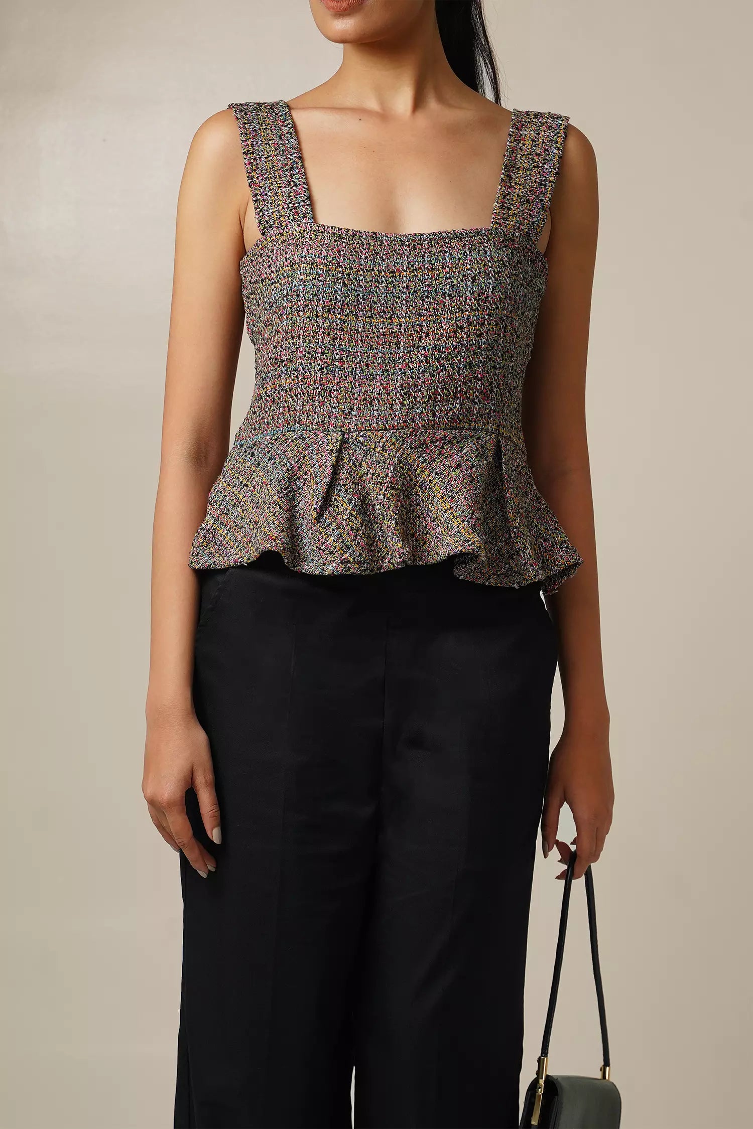 close up front view of Woman wearing a multi coloured sleeveless tweed top with square neckline and peplum bottom and black pants with a beige background